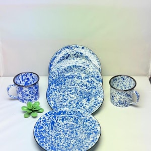 May include: A set of blue and white speckled enamelware dishes and mugs. The set includes plates and mugs with a black rim. A green succulent plant is also in the image.