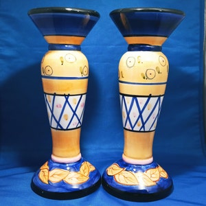 May include: A pair of ceramic candle holders with a blue, yellow, and white painted design. The holders feature a geometric pattern and leaves.