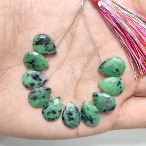 Puede incluir: Un hilo de nueve piedras preciosas de zoisita facetadas en forma de pera, con una base verde vibrante, inclusiones negras distintivas y pequeñas manchas de rubí rosa intenso, rematado con una borla de seda multicolor.