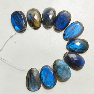 Peut inclure: Une chaîne de dix perles de pierres précieuses labradorite facettées. Les perles ovales présentent un mélange de couleurs bleues, grises et dorées. Chaque perle est enfilée sur un fil fin argenté, mettant en valeur l'iridescence naturelle.
