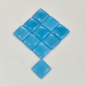 May include: Ten light blue, square glass tiles arranged in a diamond pattern. The tiles have a glossy finish and are evenly spaced. These tiles are likely for mosaic or craft projects. Each tile is approximately 2.5 cm x 2.5 cm.