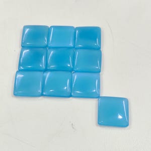 May include: Eleven square, light blue gemstones are displayed. Ten are arranged in a grid, with one separate. The stones have a smooth, polished surface and a slight translucence, reflecting light.