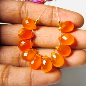 May include: A strand of orange gemstone beads, each bead is faceted and shaped like a teardrop. The beads are strung on a silver wire with gold spacers.