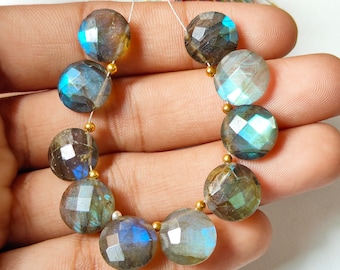 May include: A strand of faceted, round labradorite beads. The beads are primarily gray with flashes of blue and green iridescence. Small gold-colored beads separate each labradorite bead. A colorful tassel is visible in the background.