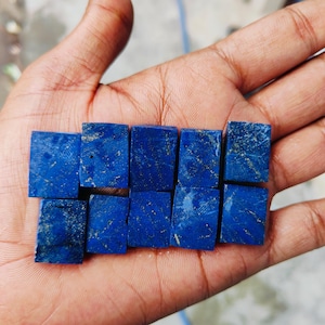 Könnte beinhalten: Eine Sammlung von neun kleinen, quadratischen Lapislazuli-Steinen. Die Steine sind tiefblau mit goldenen Pyrit-Flocken.