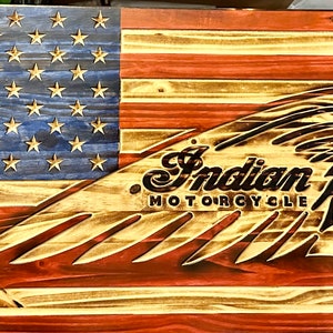 May include: A wooden American flag with the Indian Motorcycle logo in the center. The logo is a profile of an American Indian wearing a headdress with a feather and the words "Indian Motorcycle" below.
