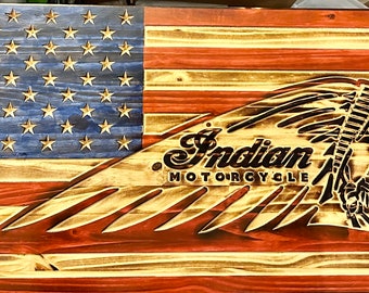 Op de afbeelding: Een Amerikaanse vlag van hout met het Indian Motorcycle logo in het midden. Het logo is een profiel van een Amerikaanse indiaan met een hoofdtooi met een veer en de woorden "Indian Motorcycle" eronder.