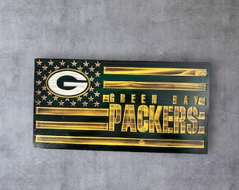 May include: Wooden Green Bay Packers flag with a distressed finish. The flag features the team's logo, stars, and the words "GREEN BAY PACKERS" in gold lettering. The flag is rectangular and mounted on a gray background.