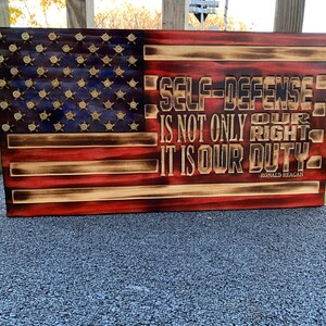 May include: A wooden American flag with bullet casings embedded in the stars. The flag is burned and distressed. The quote "Self-defense is not only our right, it is our duty." - Ronald Reagan is printed on the flag.