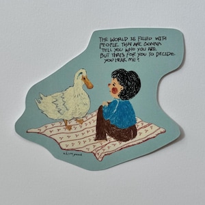 May include: A light blue sticker featuring a white duck and a person with dark hair wearing a blue shirt and brown trousers sitting on a patterned blanket. The text reads: THE WORLD IS FILLED WITH PEOPLE THAT ARE GONNA TELL YOU WHO YOU ARE BUT THAT'S FOR YOU TO DECIDE YOU HEAR ME?