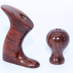 May include: Two wooden handles for a woodworking tool. The handles are made of dark wood with a reddish brown color and a grain pattern. The larger handle is shaped like a curved, open hand. The smaller handle is round and has a small hole in the top.