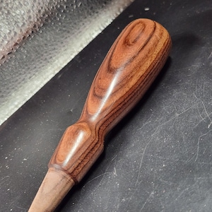 May include: A wooden handle with a dark brown and reddish brown wood grain pattern. The handle is smooth and polished.