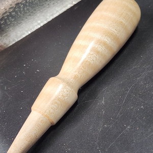 May include: A light brown wooden mallet with a tapered handle and a rounded head. The wood has a natural grain pattern.