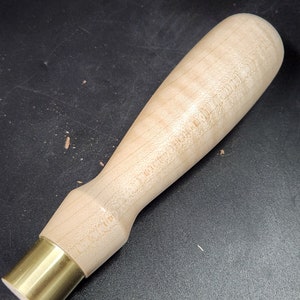 May include: A wooden handle with a brass ferrule. The handle is light brown and has a smooth finish. The ferrule is shiny and gold.