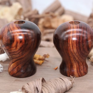 May include: Two wooden knobs with a dark brown and reddish-brown wood grain. The knobs are round with a slightly tapered bottom.