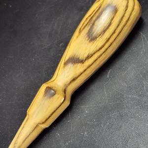 May include: A wooden chisel handle with a light brown and dark brown wood grain pattern.