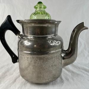 May include: A silver coffee pot with a black handle and a green glass lid. The pot has a rounded body and a spout on the side.
