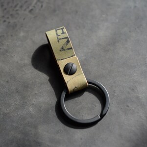 May include: A black leather key chain with a green and black patterned strap and a black metal ring. The strap has the word "ZEN" printed on it.