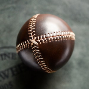May include: A brown leather baseball with white stitching. The ball is stitched in a traditional baseball pattern.