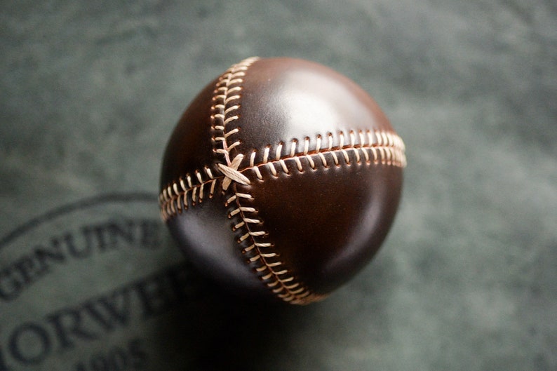 May include: A brown leather baseball with white stitching. The ball is stitched in a traditional baseball pattern.
