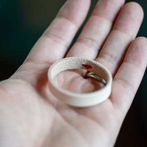 May include: A white leather ring with a small red stain on the inside.