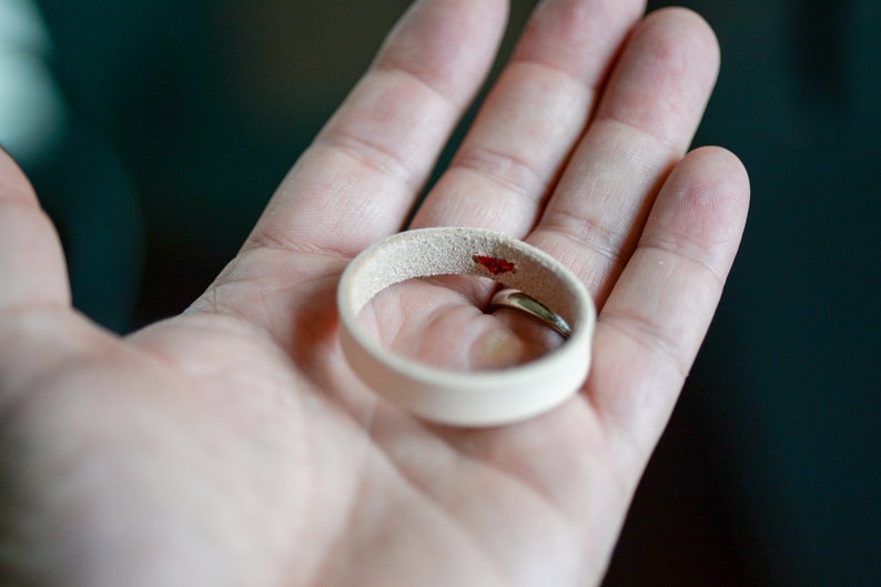 May include: A white leather ring with a small red stain on the inside.