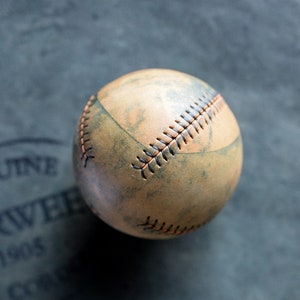 May include: A vintage baseball with brown leather and orange stitching. The ball has a worn, distressed look.