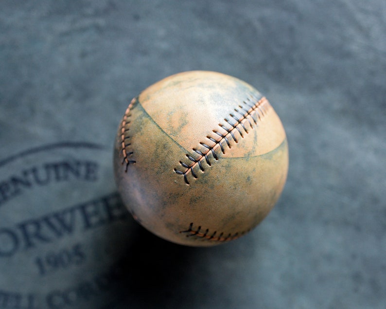 May include: A vintage baseball with brown leather and orange stitching. The ball has a worn, distressed look.