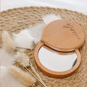 May include: A wooden compact mirror with a round, slightly oval shape. The mirror is closed and the top is engraved with the name "Molly".