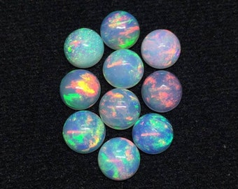 May include: A collection of nine round opals, each displaying a milky white base with iridescent flashes of color. The opals exhibit a range of hues, including green, blue, orange, and pink, against a dark background. These gemstones are ideal for jewelry making.