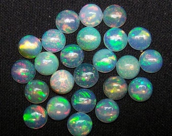 May include: A collection of round, iridescent opals. The opals display a range of colors, including blue, green, and flashes of red and yellow. The gemstones are set against a dark, textured background.