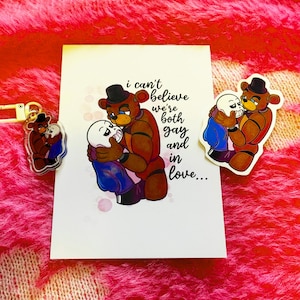 May include: A white card with the text "I can't believe we're both gay and in love..." features a cartoon bear hugging a skeleton character. A matching sticker and keychain are also visible, all with the same design.