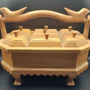 May include: A light brown wooden condiment server with an octagonal base, four short legs, and a central handle featuring carved bird silhouettes at each end. The server includes five individual lidded compartments with small knobs.