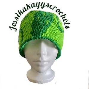 May include: A handmade crochet beanie in shades of green, with a darker green trim. The text "Jessikakayyscrochets" is arched above the beanie. The beanie is displayed on a white mannequin head.