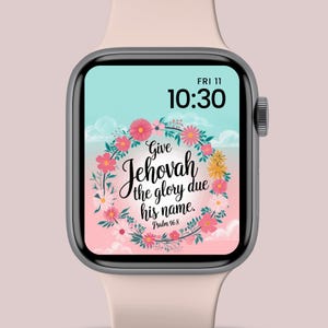 Op de afbeelding: Een zilveren smartwatch met een lichtroze band toont een bloemenontwerp met de tekst "Give Jehovah the glory due his name. Psalm 96:8." De tijd is 10:30 uur en de datum is vrijdag de 11e.