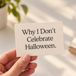 Può includere: Un cartoncino rettangolare color bianco sporco con una superficie testurizzata che riporta il testo stampato in nero Why I Don't Celebrate Halloween. Il cartoncino è tenuto in modo da mostrare chiaramente il messaggio su uno sfondo neutro.