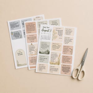 Può includere: Tre fogli di carta con un calendario di testi giornalieri per agosto, stampati con citazioni ispiratrici, date e piccole illustrazioni botaniche in tonalità terra tenui. Un paio di forbici in metallo argentato si trova a destra dei fogli.