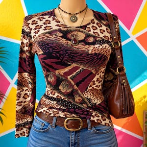 May include: A long-sleeve top featuring a multi-patterned design with leopard print, black, and deep burgundy sections. The garment is paired with blue denim jeans, a brown leather belt with a gold buckle, and a brown leather shoulder bag.