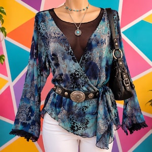 May include: A long-sleeved wrap blouse in shades of blue, teal, and black with a mottled pattern, featuring a black mesh neckline insert, a black leather belt with a large silver-toned metal buckle, and a black shoulder bag with silver hardware.