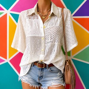 May include: A white short-sleeved button-down shirt featuring a patchwork design of various lace and eyelet fabrics. The shirt is paired with light blue distressed denim shorts, a brown leather belt with a gold buckle, and a brown fringe bag.