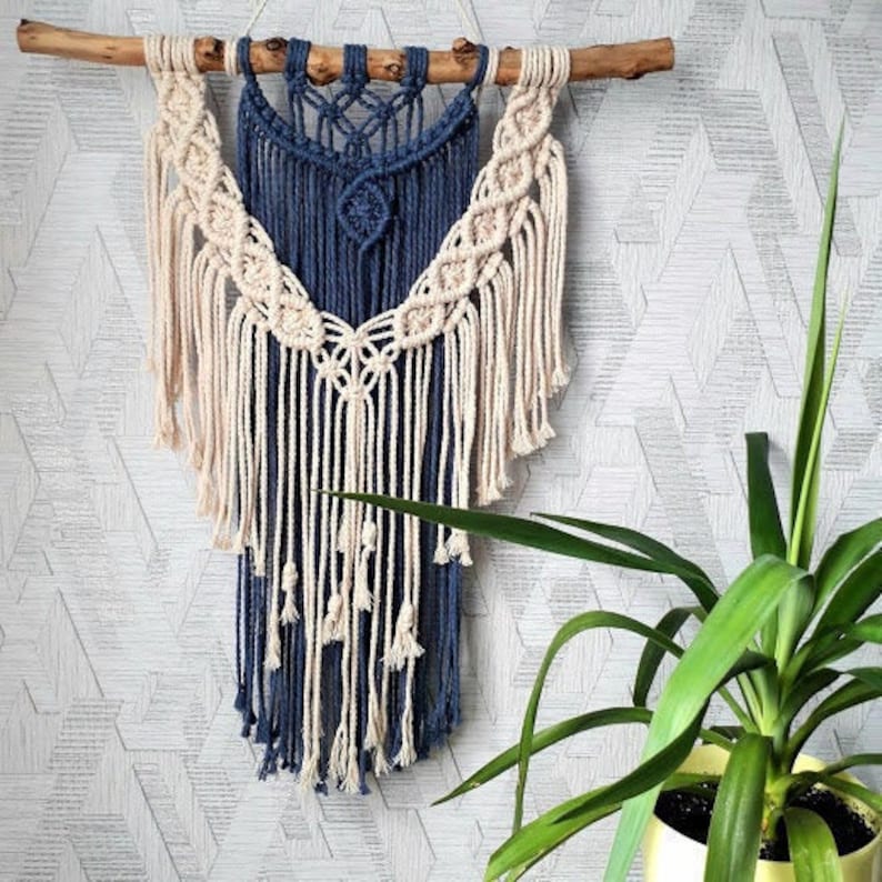 Pu&ograve; includere: Un arazzo da parete in macram&egrave; blu e bianco con un motivo geometrico. L'arazzo &egrave; realizzato in cordoncino di cotone e ha una frangia sul fondo.