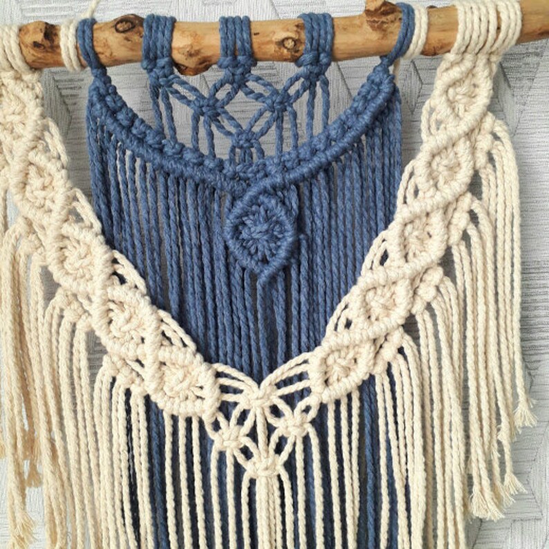Pu&ograve; includere: Un arazzo da parete in macram&egrave; con uno schema di colori blu e bianco. L'arazzo presenta un grande disegno circolare al centro e una variet&agrave; di nodi e frange.