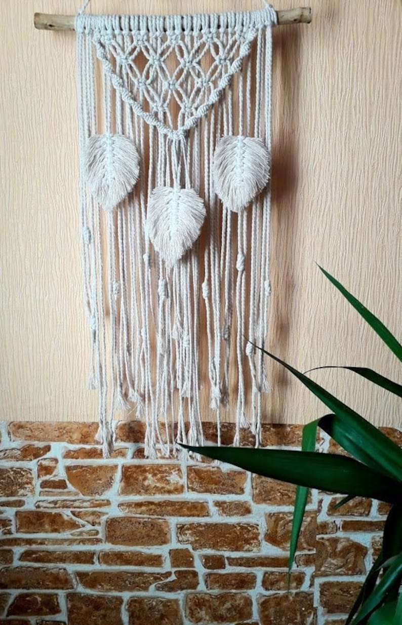 Peut inclure: Une suspension murale en macram&eacute; blanche avec un motif g&eacute;om&eacute;trique et trois accents en forme de plumes.