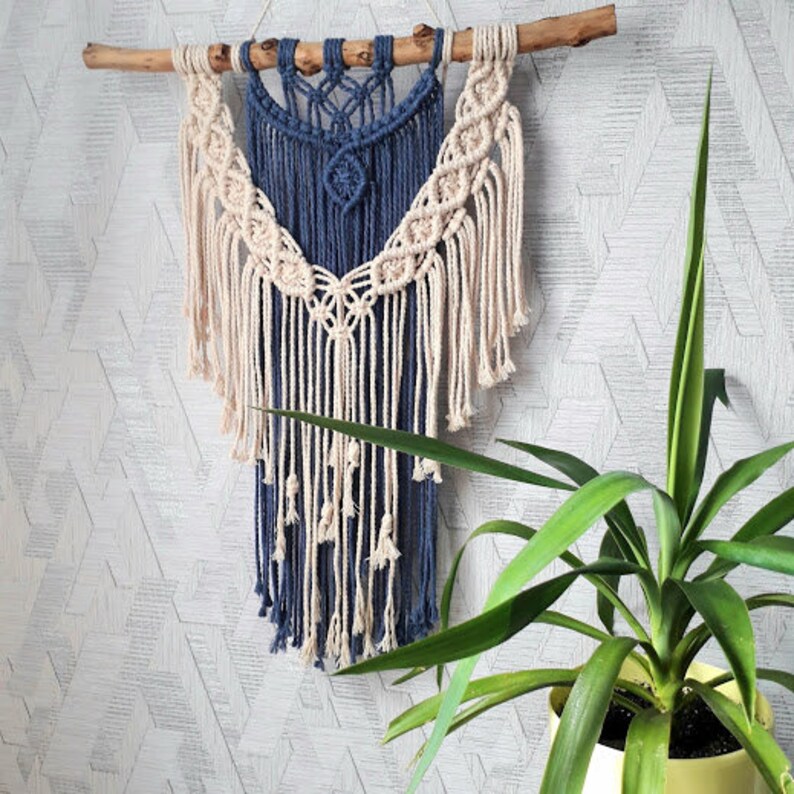 Pu&ograve; includere: Un arazzo da parete in macram&egrave; blu e bianco con un motivo geometrico. L'arazzo &egrave; realizzato con cordoncino di cotone e ha una frangia sul fondo.