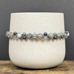 May include: A gray beaded bracelet with a mix of round and faceted beads, including moonstone, agate, and hematite.
