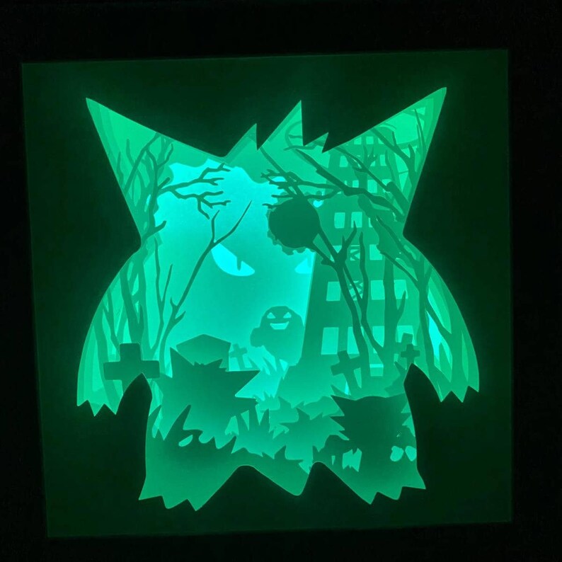 May include: A green glow-in-the-dark papercraft of a spooky ghost with trees and a building in the background.