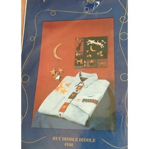 May include: A light blue denim shirt with a decorative design featuring moons and stars. The shirt has a button-down front and long sleeves. The image also includes a framed artwork with a similar celestial theme. The text "HEY DIDDLE DIDDLE #104" is at the bottom.