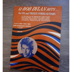 May include: Sheet music titled "12 Bob Dylan Hits for Six and Twelve String Guitars." The cover is orange with black and white wavy lines. A circular image of Bob Dylan is in the center. Song titles are listed.
