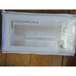 May include: A white plastic package containing a Lisette rod-pocket panel by JCP Home. The packaging features a clear window displaying a beige curtain with a horizontal slat design and a label indicating an 84 inch length for the curtain panel.