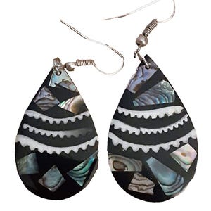 May include: A pair of teardrop-shaped earrings featuring a black base inlaid with iridescent abalone shell fragments and two horizontal white scalloped lines. Each earring hangs from a silver-toned metal hook wire with a small coiled spring detail.